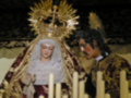 Imagen religiosa de una Virgen con un niño en un entorno oscuro, rodeada por velas y vestimenta tradicional.