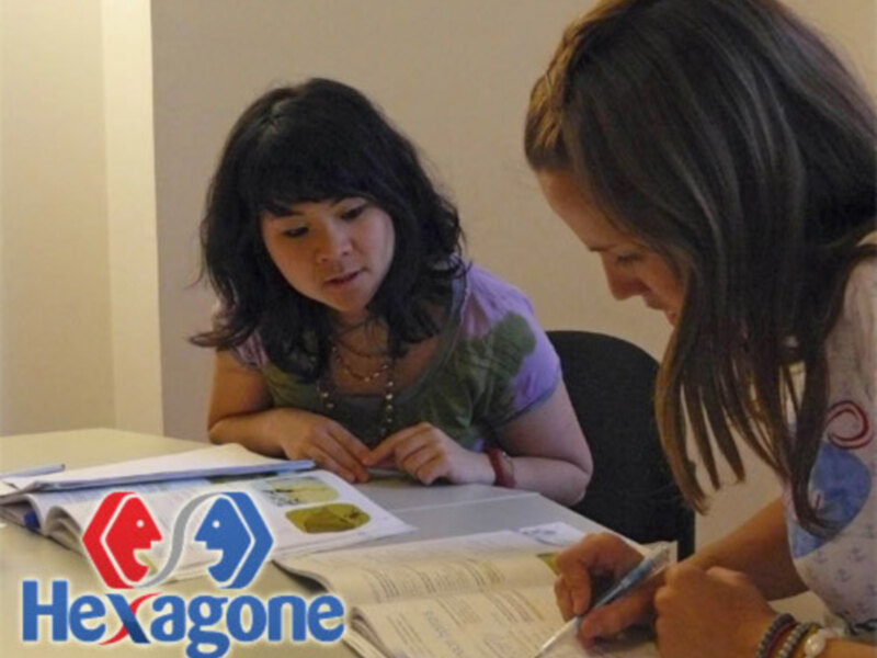 Dos personas estudiando juntas, con libros y material escolar en una mesa.