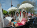 Parade with women in traditional attire and white lace umbrellas.