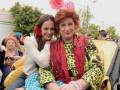 Dos personas participan en un desfile, una con flores rojas y otra con un disfraz de payaso.