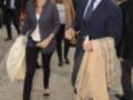 Una pareja camina por una calle con un hombre vestido de negro y una mujer con blazer azul. La imagen parece ser de una celebridad en un evento formal.