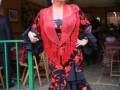 Una mujer vestida con un traje de flamenco tradicional, posando frente a una decoración festiva.