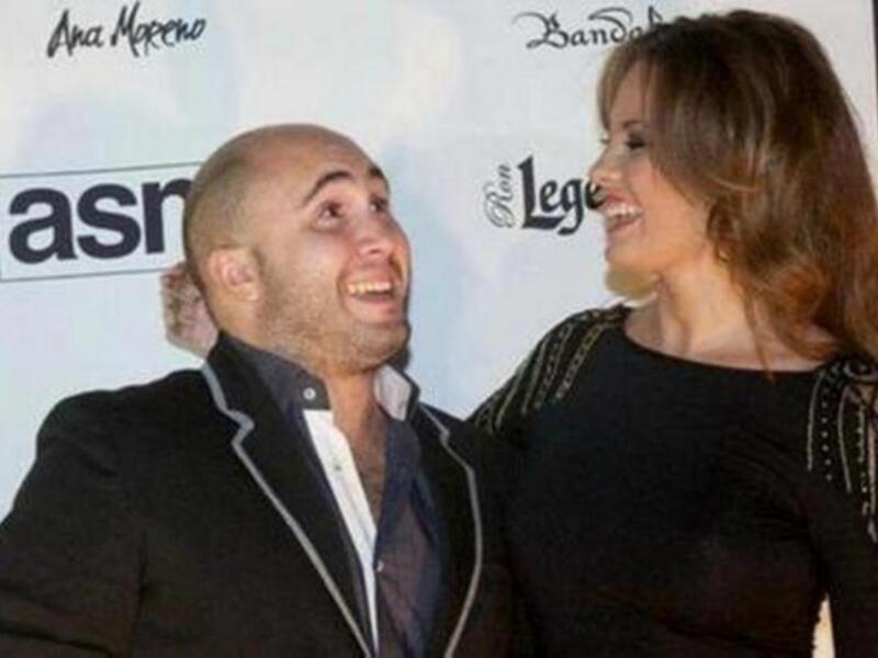 Persona masculina y femenina sonrientes en un evento, fondo con logotipos de 'Ana Moreno' y 'Ron Legend'.