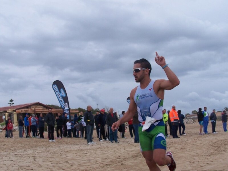 Atleta corriendo en una carrera de triatlón en la playa, con un entusiasta público al fondo.