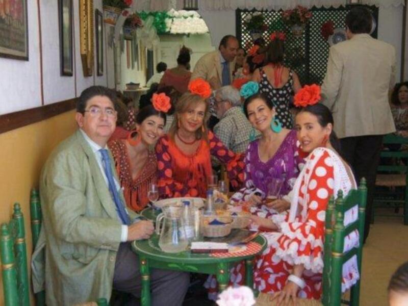 Grupo de personas en trajes típicos de Andalucía, posando en una mesa con decoración festiva.
