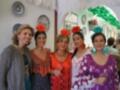 Las mujeres están vestidas con trajes típicos españoles de la Feria de Abril, posando en un ambiente festivo con decoración verde y azul.