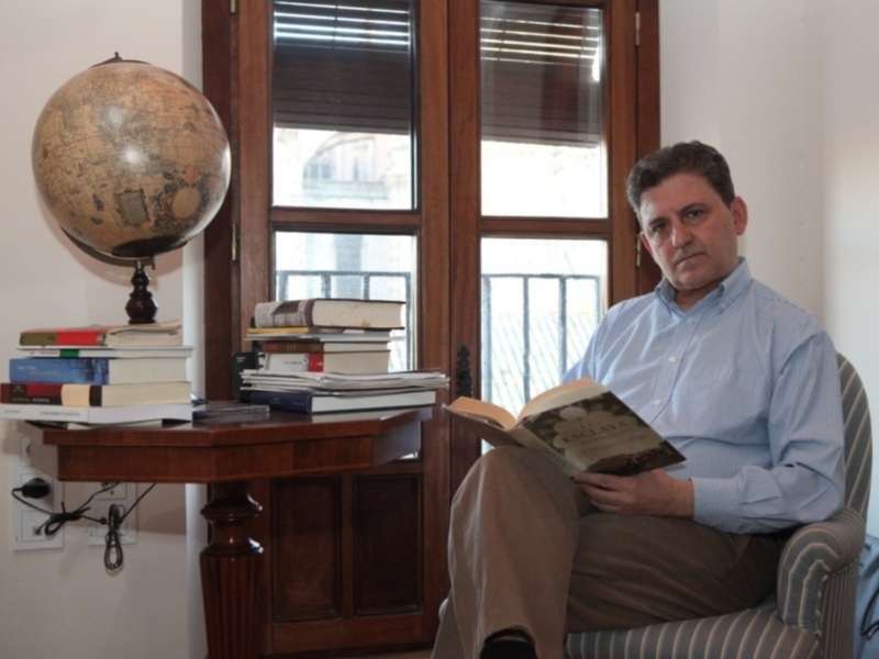 Hombre leyendo un libro en un sillón, rodeado de libros y un globo terráqueo en una estantería.