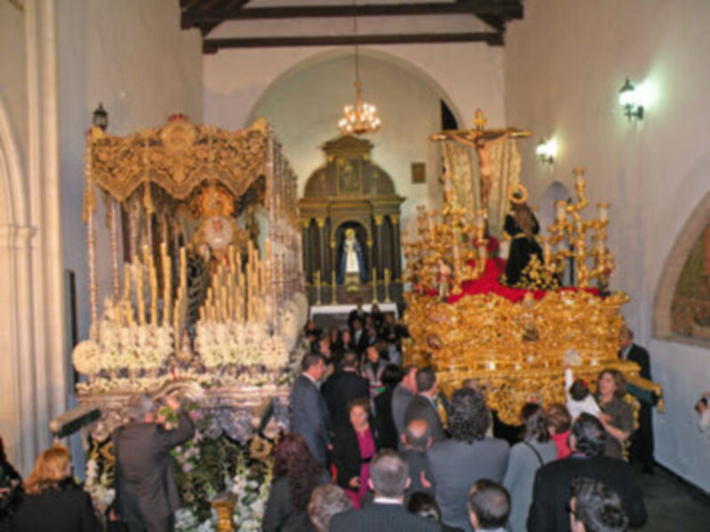 Una procesión religiosa en una iglesia, con una imagen de la Virgen en el altar y una multitud de personas participando en la ceremonia.
