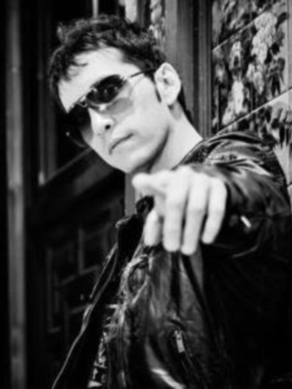 Un hombre con gafas de sol y una chaqueta negra, apuntando hacia la cámara.