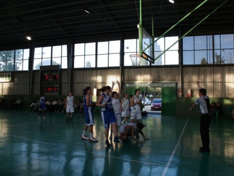 Jugadores de baloncesto femenino en acción durante un partido en una cancha cubierta con espectadores en el fondo.