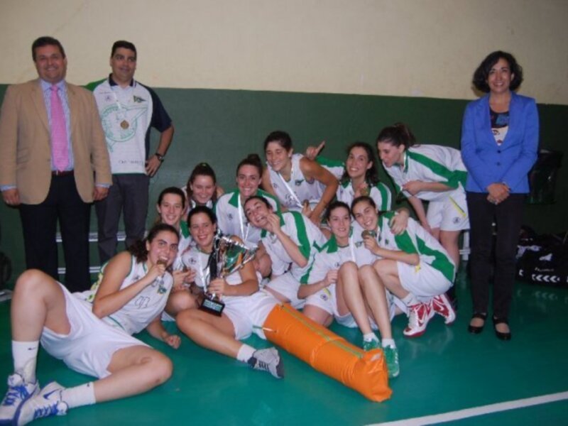 Equipo femenino de baloncesto celebrando con trofeos en una cancha de baloncesto.