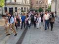 Un grupo de personas caminando por una calle con edificios históricos y farolas en el fondo.