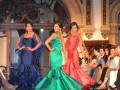 Modelos presentan vestidos de colores vibrantes en un desfile de moda. La audiencia observa con interés la presentación.