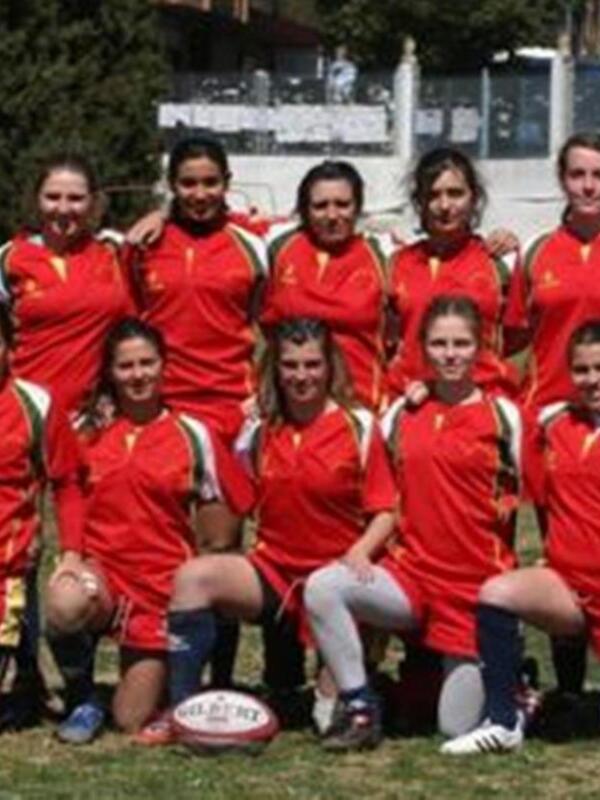 Equipo femenino de rugby en uniforme rojo, posando en un campo de juego.