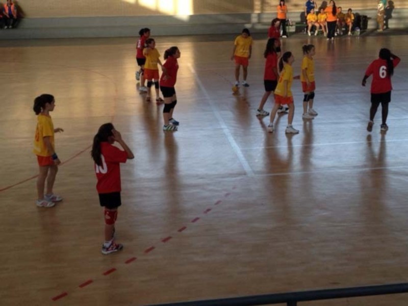 Niños jugando fútbol en un gimnasio, con líneas rojas marcando el campo de juego. Algunos niños están en el centro del campo, mientras otros están en las orillas, listos para comenzar el partido.