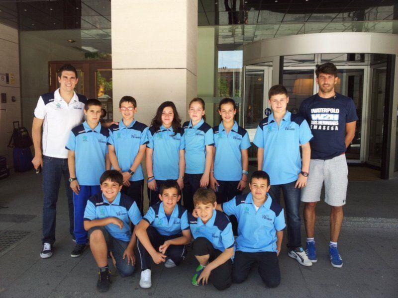 Equipo de waterpolo juvenil posando en el exterior de un edificio moderno.