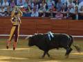 Un torero en acción durante una corrida de toros, con un toro en el ruedo y un público atento en el fondo.