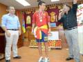 Un hombre en una camiseta de la selección española de fútbol sostiene una medalla mientras un hombre con micrófono lo felicita.