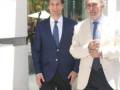 Dos hombres en trajes de negocios caminan juntos, uno con un traje azul y corbata azul, el otro con un traje beige claro y corbata azul.