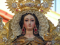 Figura de la Virgen María con ornamentos dorados y rojos, representando un aspecto religioso y festivo.