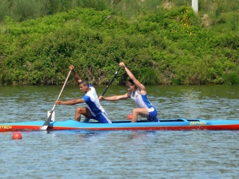 Dos personas remando en una canoa azul en un lago con vegetación al fondo.