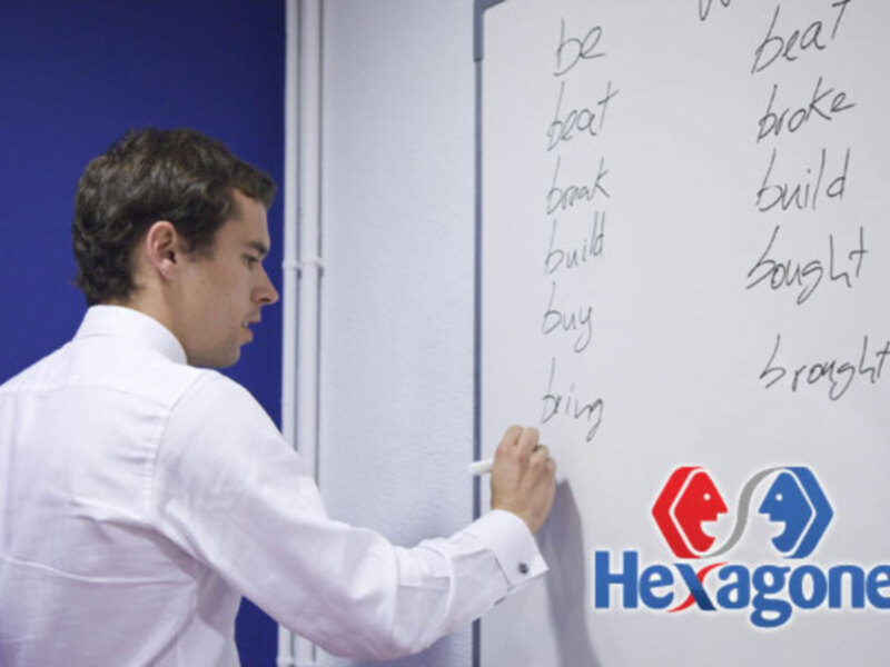 Persona escribiendo en una pizarra con palabras de conjugación de verbos en inglés.