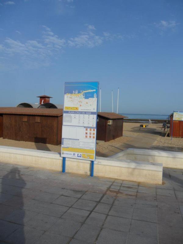 Placa informativa en la playa Cruz del Mar, con mapa y calendario, bajo un cielo azul claro.