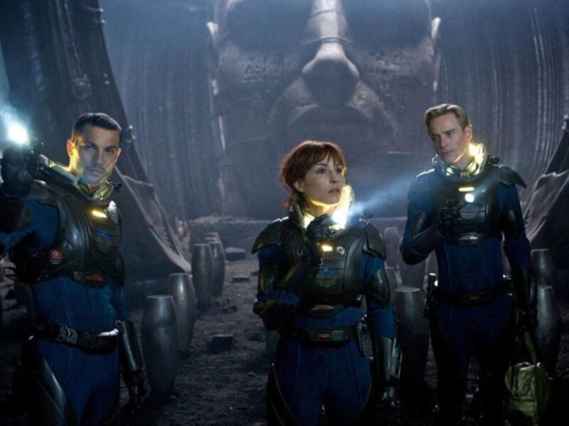 Tres personajes en trajes espaciales con lámparas de mano, posiblemente en una nave espacial o entorno futurista.