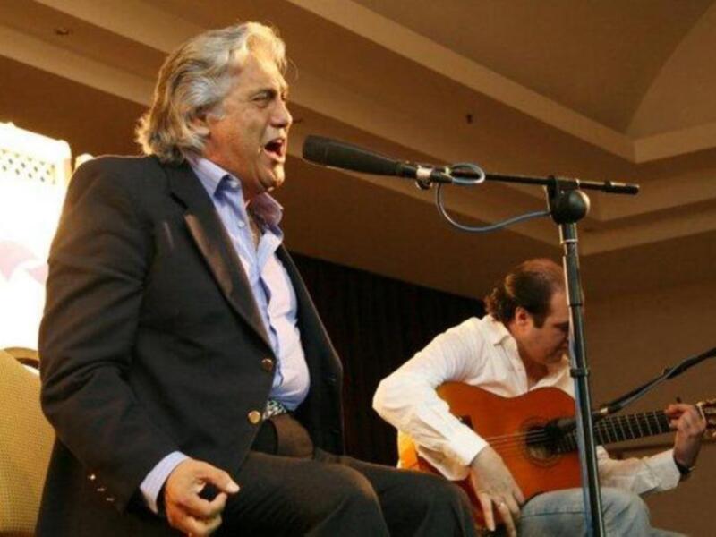 Un músico en traje canta mientras otro toca la guitarra clásica en un escenario.