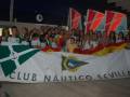 Una multitud de personas sonríe y celebra junto a un gran banner que contiene el nombre del Club Náutico de Sevilla.