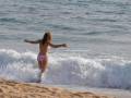 Una mujer en bikini está disfrutando de la onda del mar, con el agua azul y las olas rompiendo cerca de la costa.
