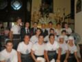 Grupo de jóvenes vestidos con uniformes blancos y negros, posando en una sala decorada con candelabros y estatuas.