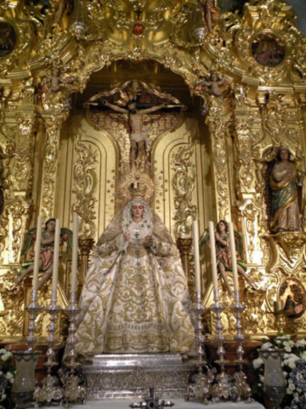 Altar con imagen de la Virgen María y Cristo crucificado, rodeado por ornamentos dorados y figuras religiosas.