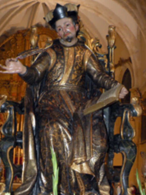 Figura de San Jorge en una iglesia, vestido con armadura dorada y sosteniendo un libro.