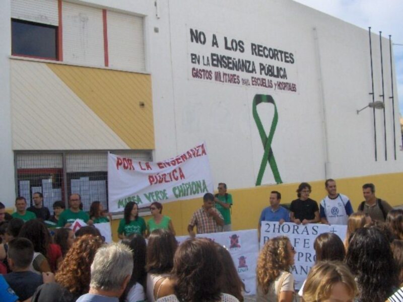 Protesta por la educación pública frente a un edificio con letreros sobre recortes y gastos militares.