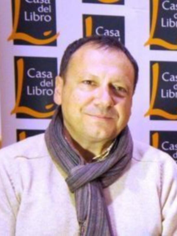 Un hombre con una bufanda blanca y una camisa de manga larga, posando frente a una bandera con el logo de Casa del Libro.