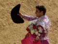 Un torero sostiene un sombrero negro y una corbata con flores, posiblemente en el campo de una corrida de toros.
