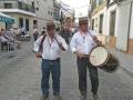 Dos músicos tocan instrumentos tradicionales en una calle de pueblo durante una celebración o festival.