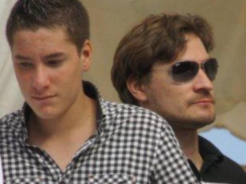 Dos personas sentadas juntas, uno con camisa a cuadros y el otro con gafas de sol.