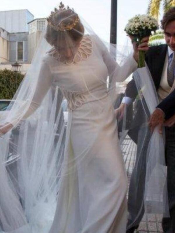 Boda en una iglesia, novia con vestido blanco y corona, novio con traje negro y corbata, ambas sonríen y son una pareja casada.