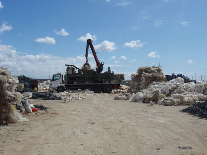 Reciclaje de residuos en un punto de recogida con un camión y grúa manipulando materiales.