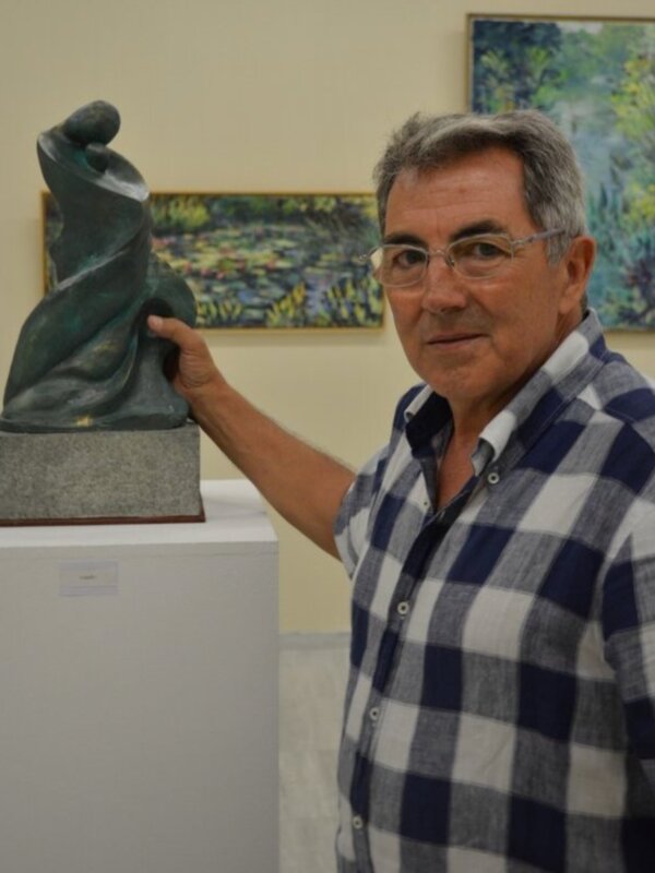 Artista posa junto a su escultura en una exposición de arte.