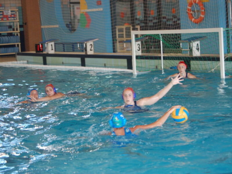 Jugadoras de waterpolo en acción durante un partido en piscina cubierta.