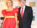 Una pareja en un evento formal, ella viste un vestido rojo con mangas puffy y él lleva un traje negro con corbata roja.