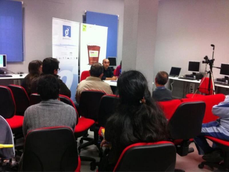 Reunión o taller en una sala de conferencias con participantes sentados y un presentador en el centro.