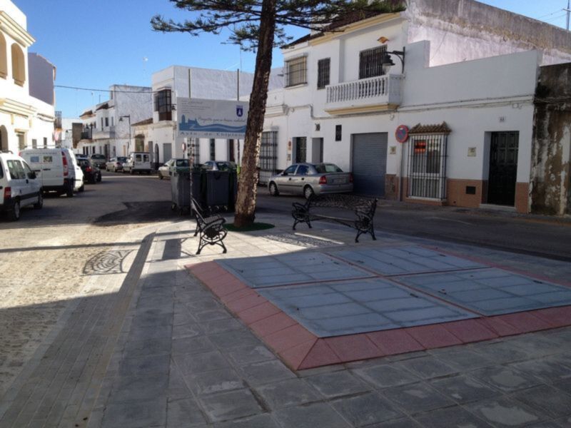 Plaza tranquila con bancos y árboles en un pueblo blanco, con calles y edificios típicos de la región.