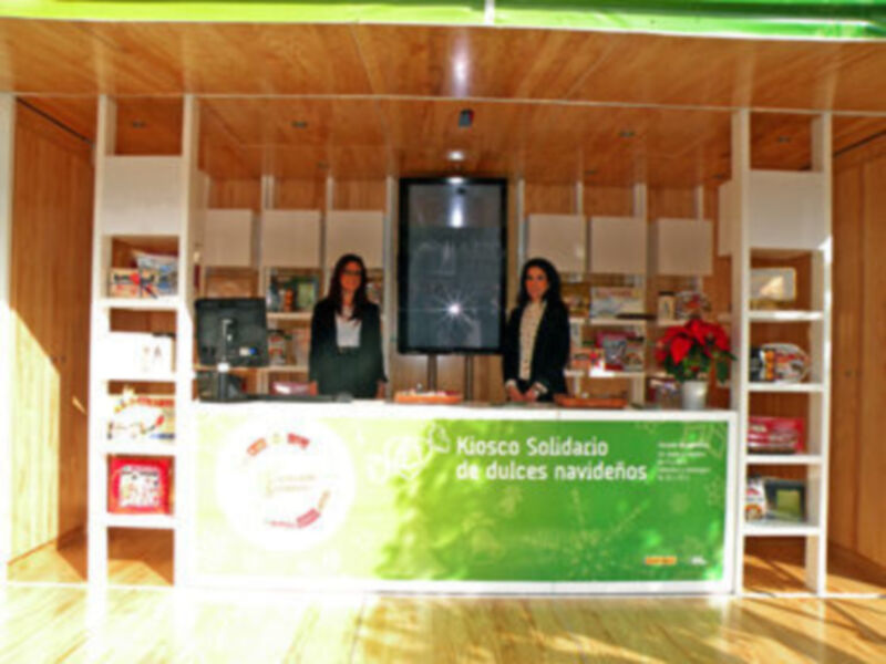 Kiosco Solidario de dulces navideños con dos personas en el interior de una casa con madera.