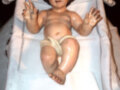 Figura de niño en trono con vestimenta blanca y mantel bordado, representación religiosa.