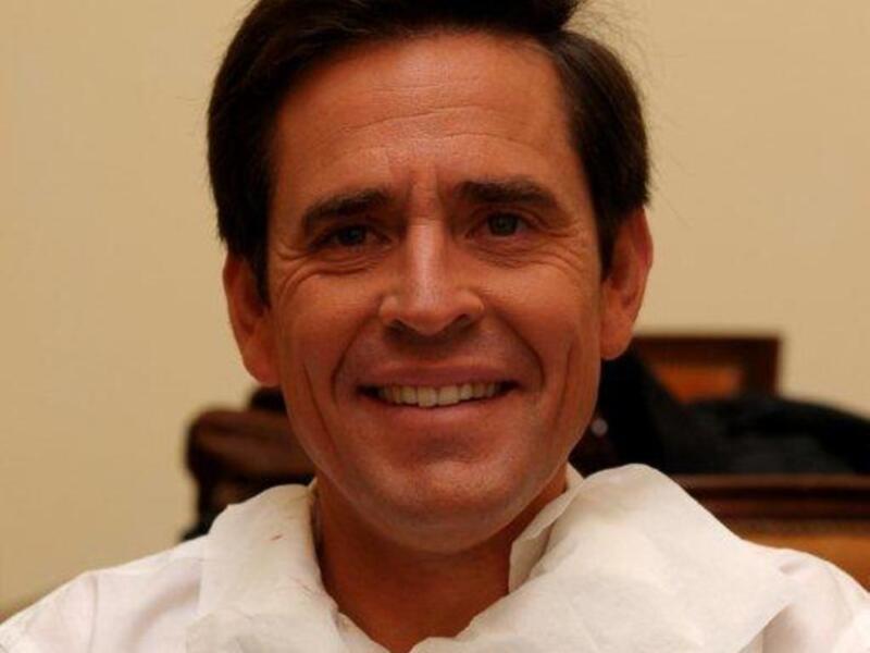 Retrato de hombre sonriente con cabello oscuro y camisa blanca.