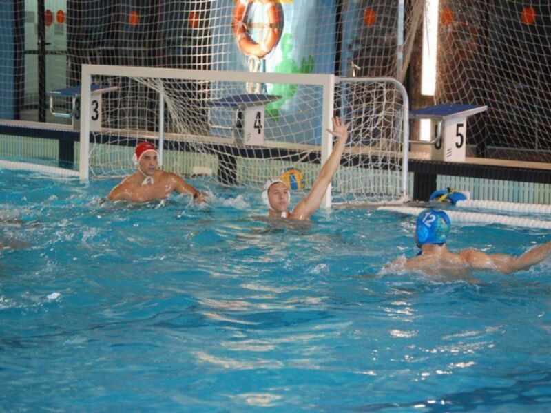 Jugadores de waterpolo en acción durante un partido en una piscina cubierta.